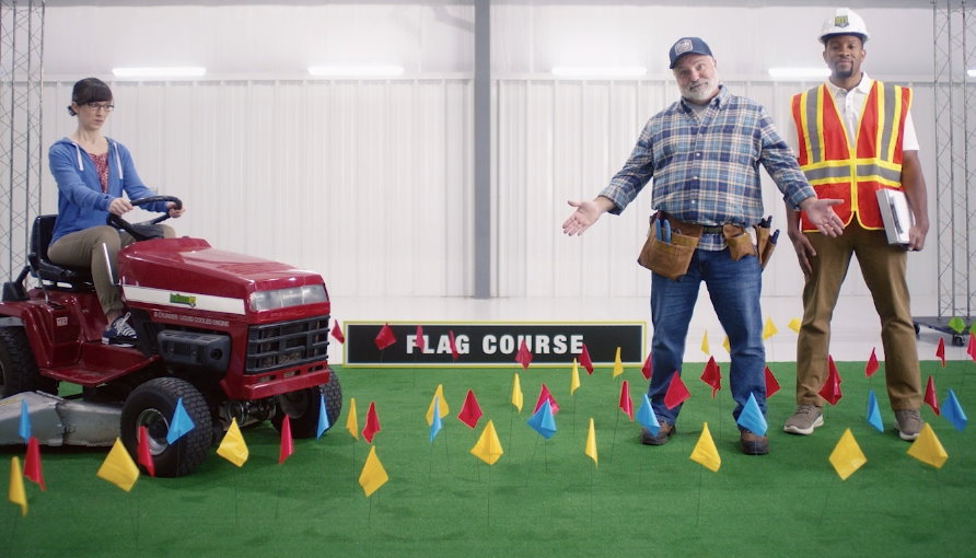 Contractor and utility worker standing with flags placed all over a yard and a woman on a riding mower